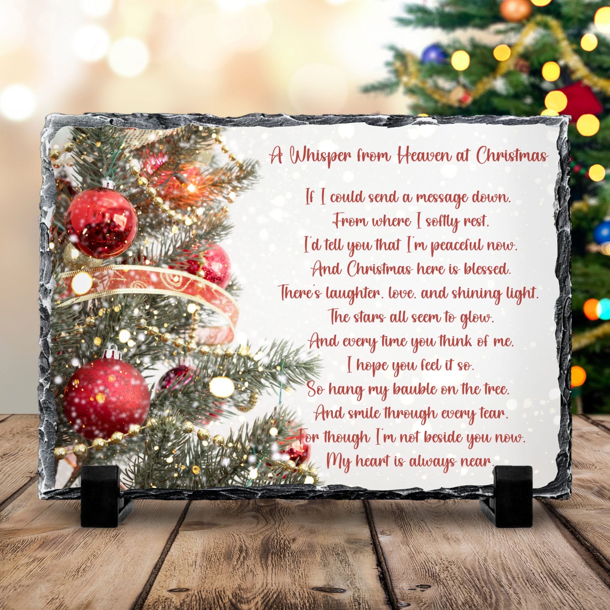 Decorative plaque with Christmas tree and poem on a wooden surface with blurred festive lights in the background.